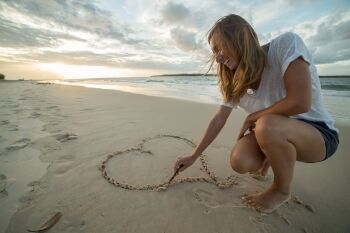 Young woman on beack drawing love heart in sand 350 233