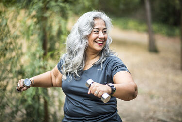 Midlife woman dumbells in park smiling exercise