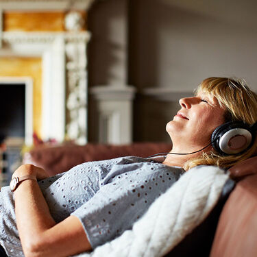 Midlife woman listening to podcast on couch relaxing